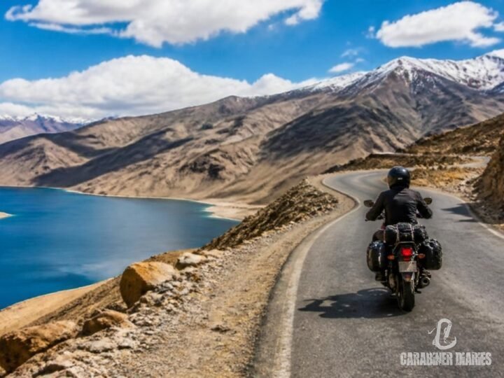 Motorbike rider on a high mountain road beside a blue lake in Ladakh