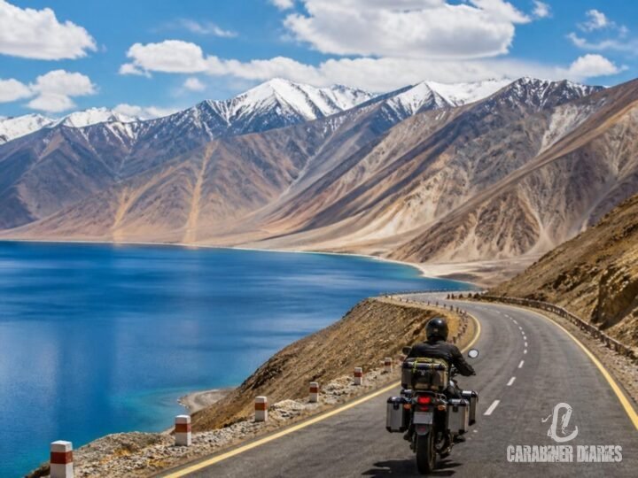 Motorbike rider on a winding Ladakh road with a blue lake and barren mountains